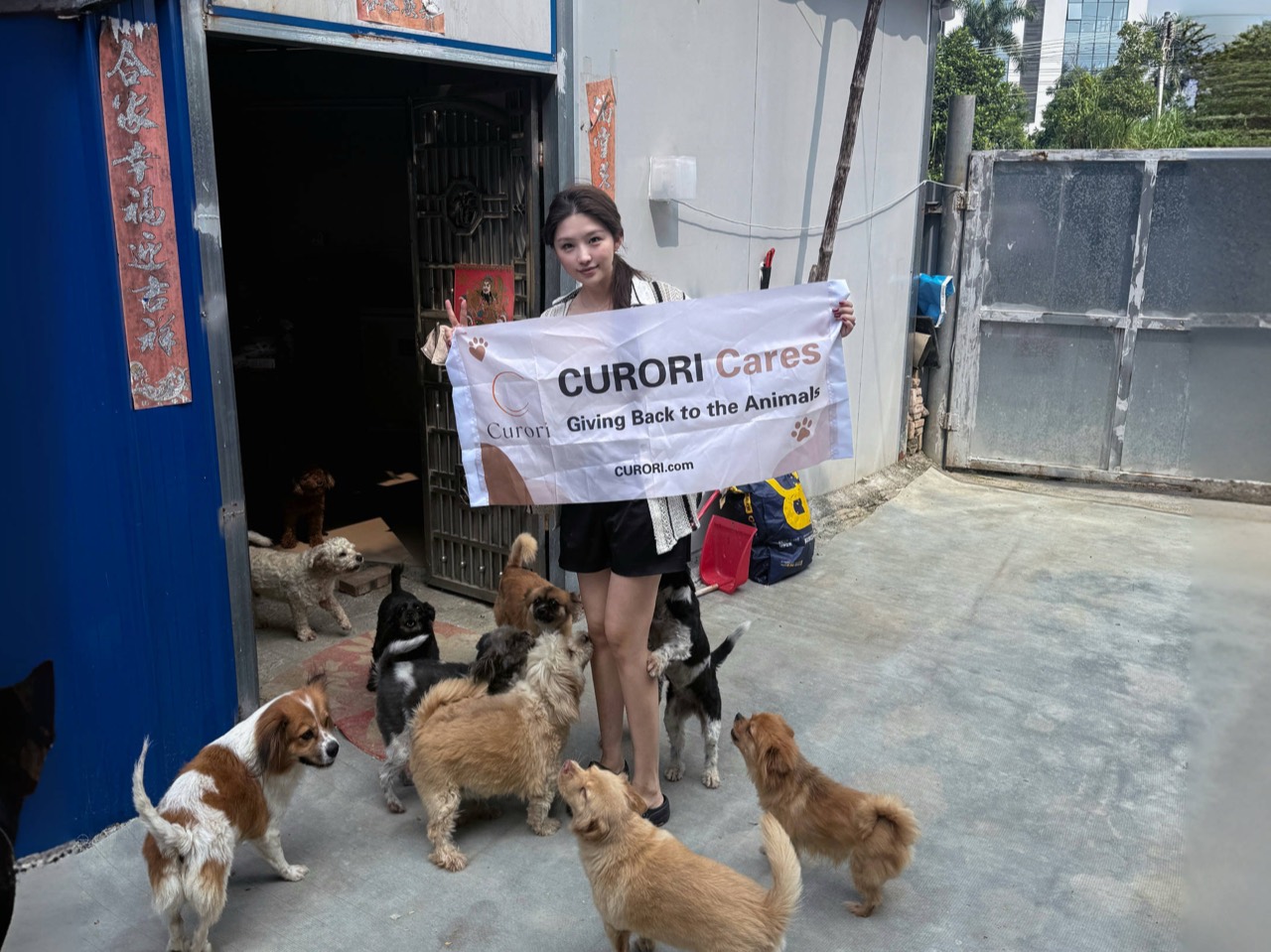 CURORI representative holding a CURORI Cares banner among rescued dogs at a Dongguan animal shelter