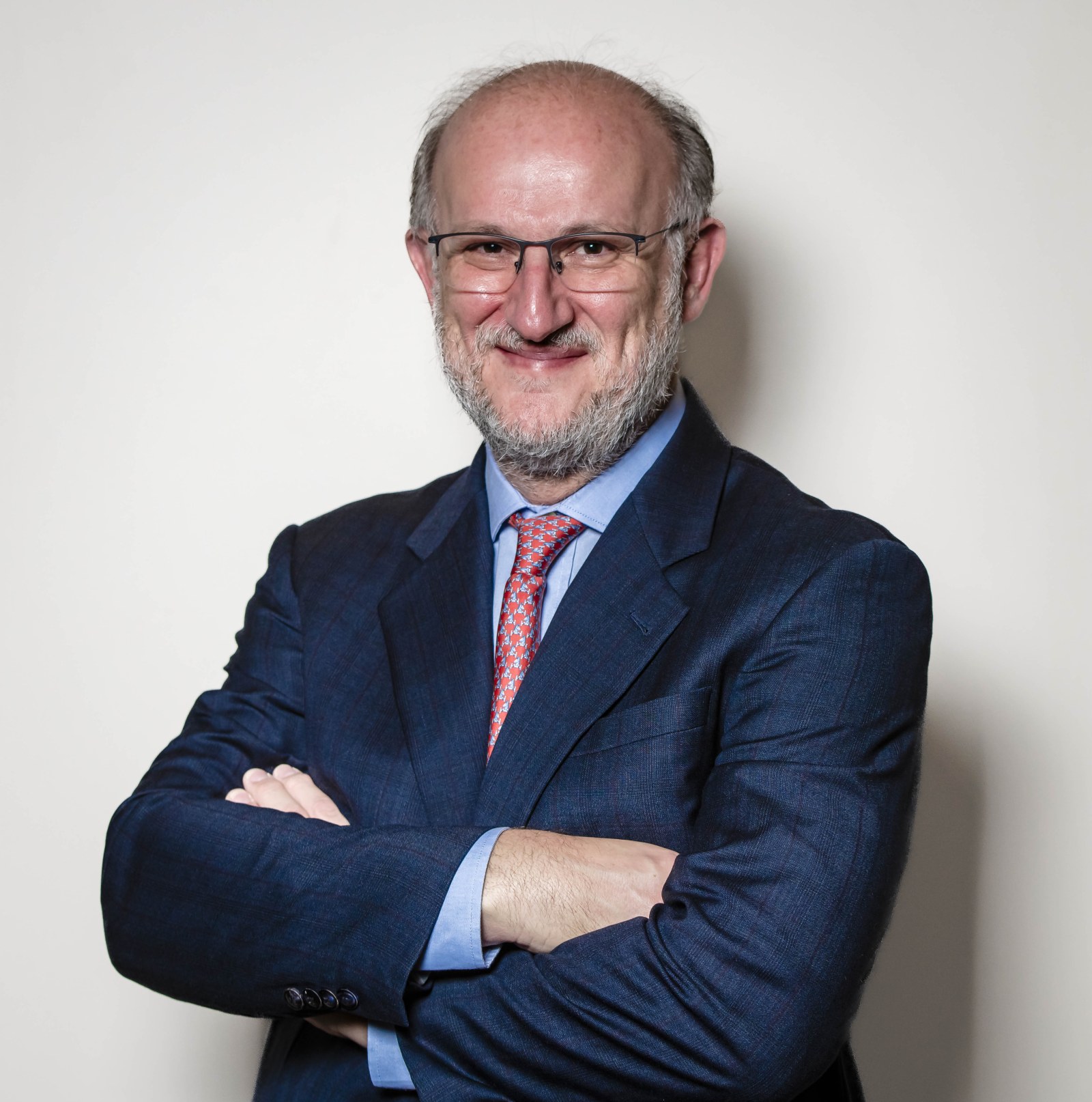 Dr. Feres Chaddad poses for a portrait wearing a navy blue suit, light blue shirt and red tie, with his arms crossed.