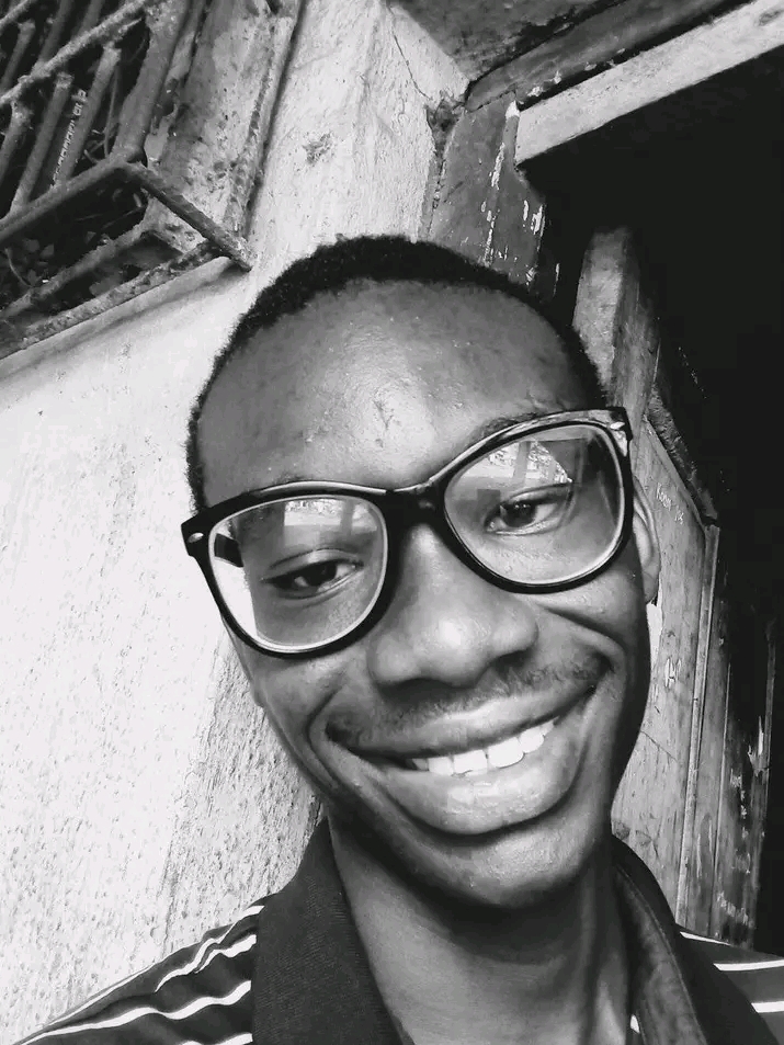 Uzopuo Miracle Ositadimma smiling wearing large, dark- frame eyesglasses. He has a closely shaved and is looking toward the camera with a cheerful expression. It's also a black and white picture